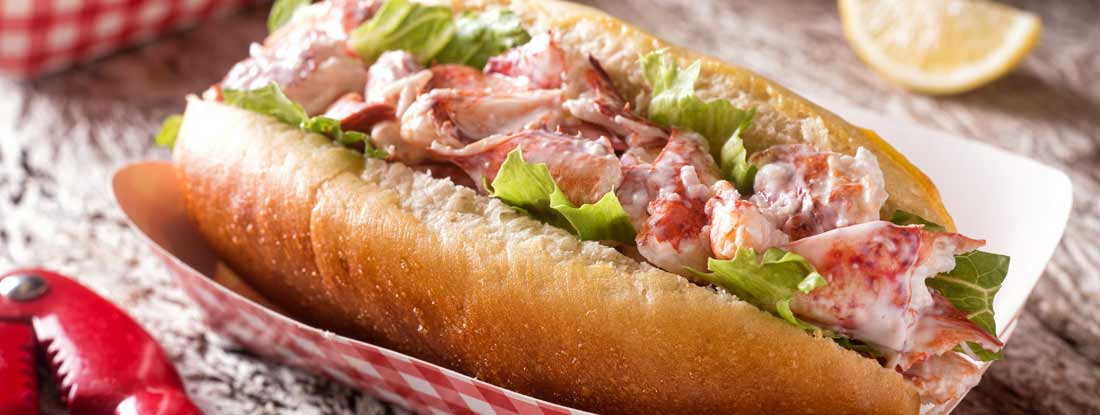 A delicious lobster roll on a rustic wood table top. Find Connecticut Restaurant Insurance.