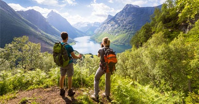 Two hikers at viewpoint in mountains with lake, sunny summer