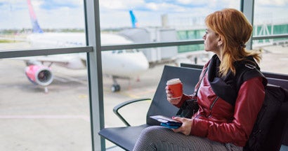 Times When Travel Insurance Is a Must-Have. Woman sitting at the gate waiting room with traveling documents and coffee.