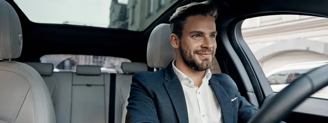 Man in full suit smiling while driving a car. How to Find the Best Car Insurance Coverage in Ellicott City, Maryland.