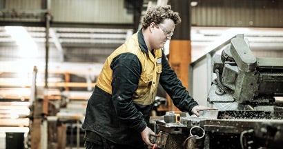 Blue collar worker in factory cutting metal parts. Workers' compensation for employees.