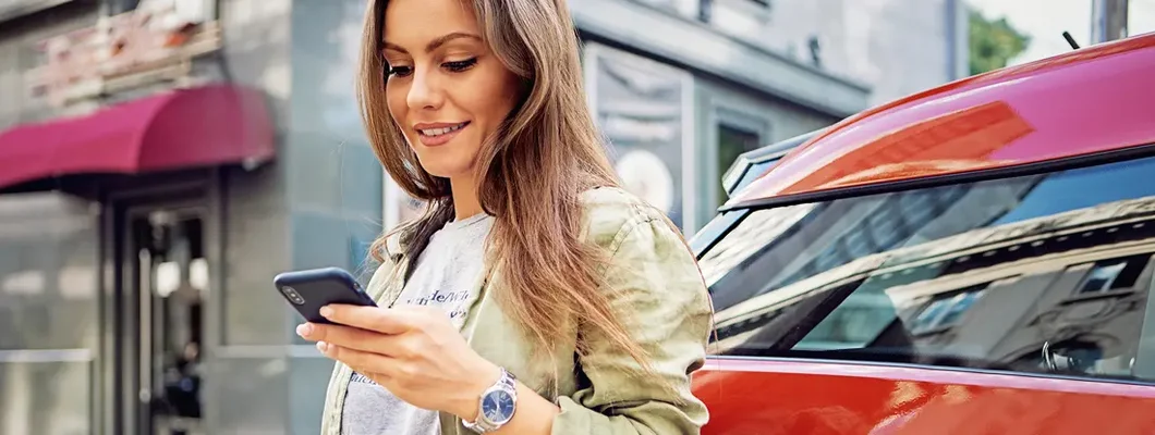 Woman using mobile phone while charging electric car. How to Find the Best Car Insurance Coverage in Fairfax, Virginia.