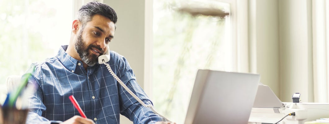 Businessman using phone and laptop at home office. Find Bluffton, South Carolina business insurance.