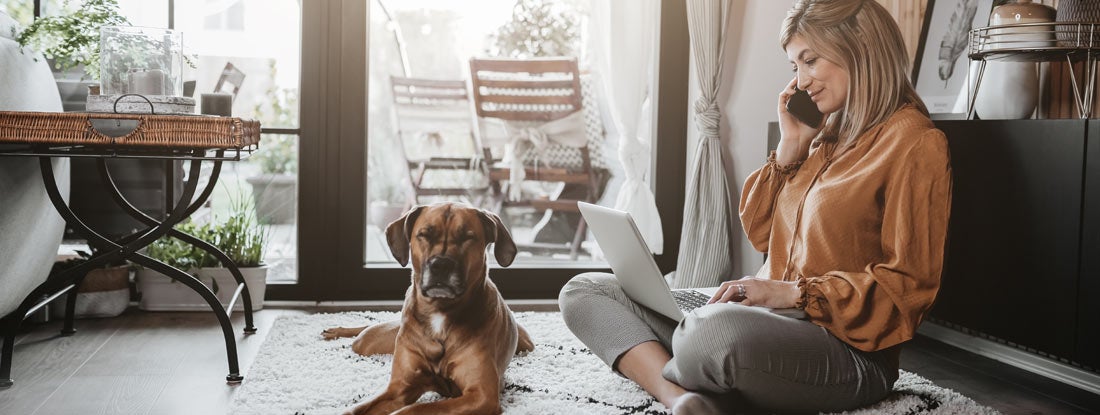Woman working from home with her dog sitting nearby. Find Pet Health Insurance.