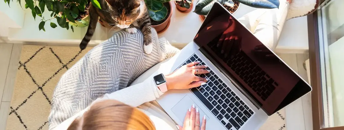 Woman working on laptop at home with cat nearby. How Does Workers' Comp Work for Remote Employees?