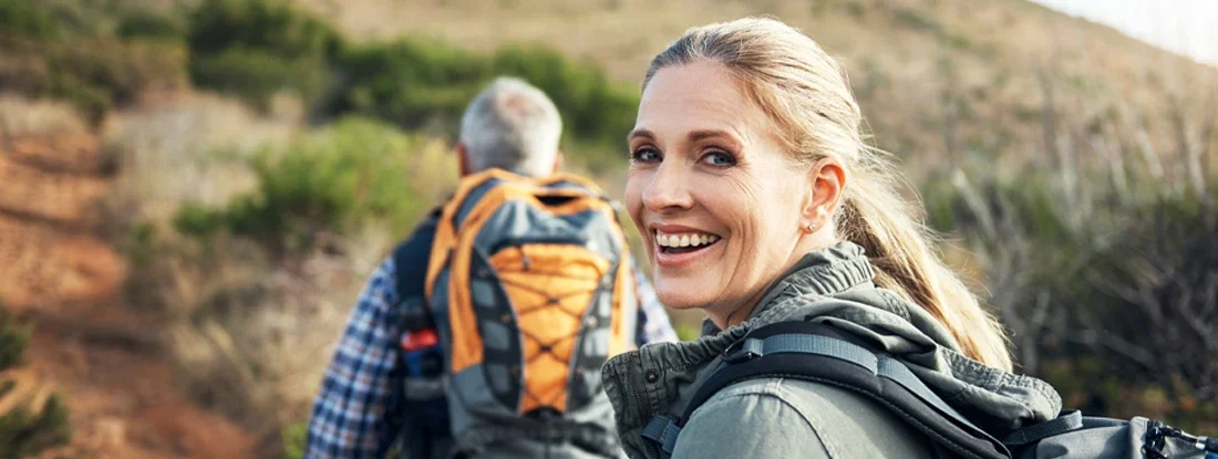 Portrait of a mature woman hiking with her husband through the mountains. Whole Life vs Term Life Insurance.