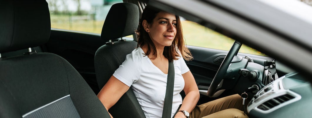 Woman sitting in a car putting on her seat belt. Find Columbia Missouri car insurance.