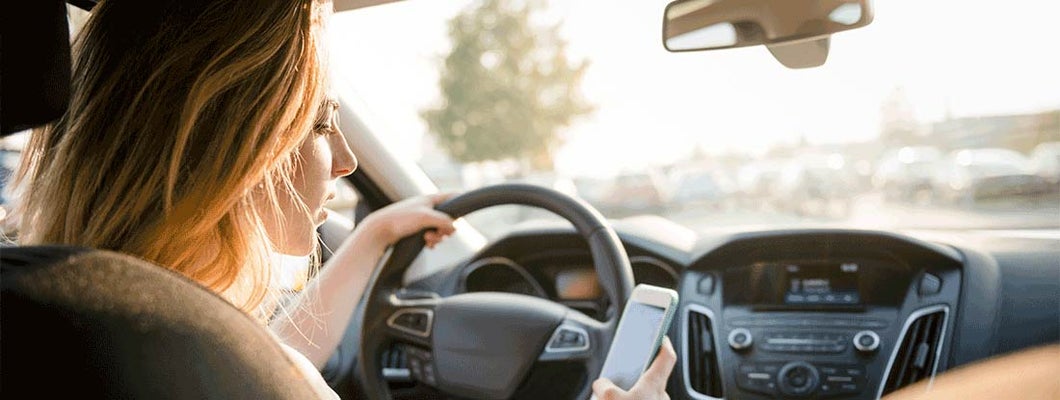 Woman looking at phone while driving. Distracted Driving Laws in Vermont.