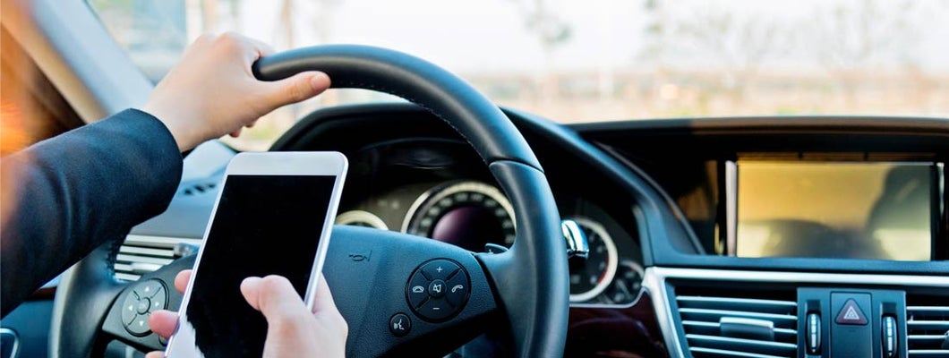 Man looking at phone while he is driving distracted. Distracted Driving Laws by State.