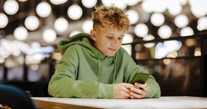 Smiling boy using smart phone in illuminated food court. Surprising New Study About Teens and Texting. 