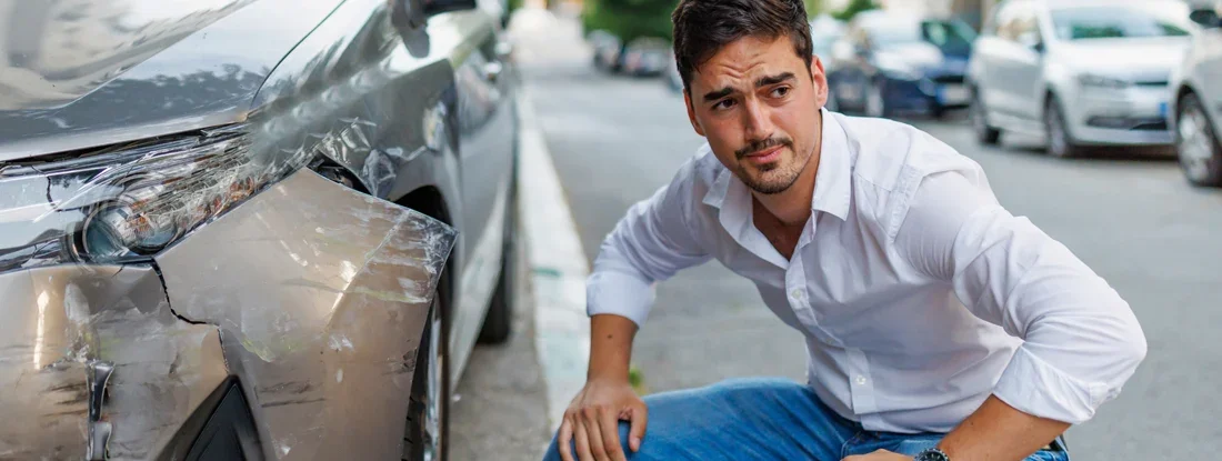 Man next to crashed car, looking away with a worried facial expression. Find Uninsured Motorist Coverage.