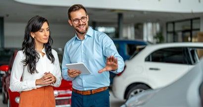 Happy salesman selling the car to his female customer in a showroom. 10 Car Buying Secrets You Need to Know.