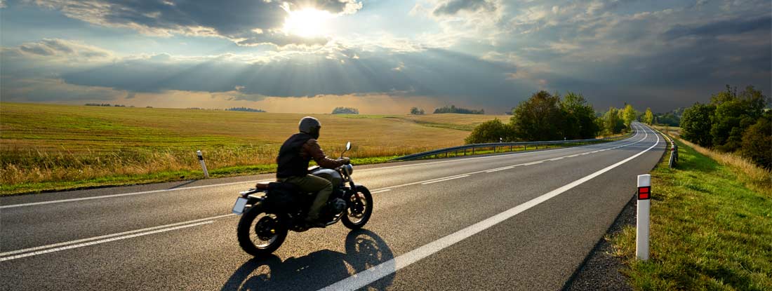 Person riding a motorcycle on a scenic country road. Find Motorcycle Liability Insurance.