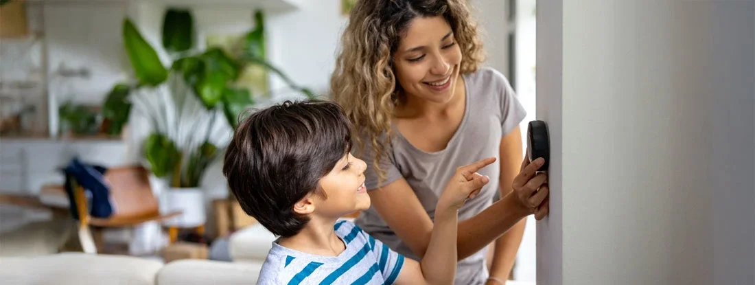 Mother and son at home using a smart thermostat. Smart Home Technology and Insurance Discounts.