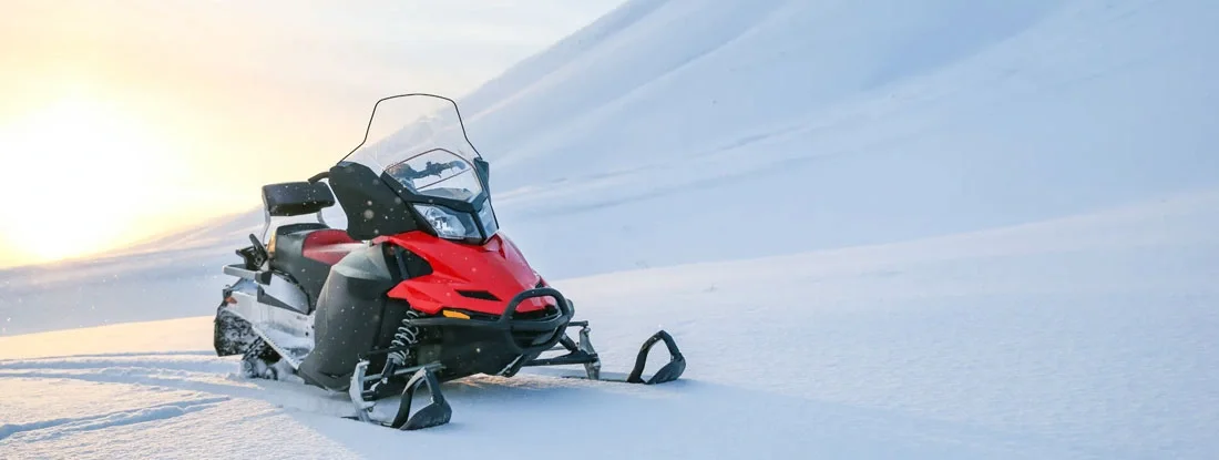 Red snowmobile on a background of snowy mountains. Find Maine Snowmobile Insurance.