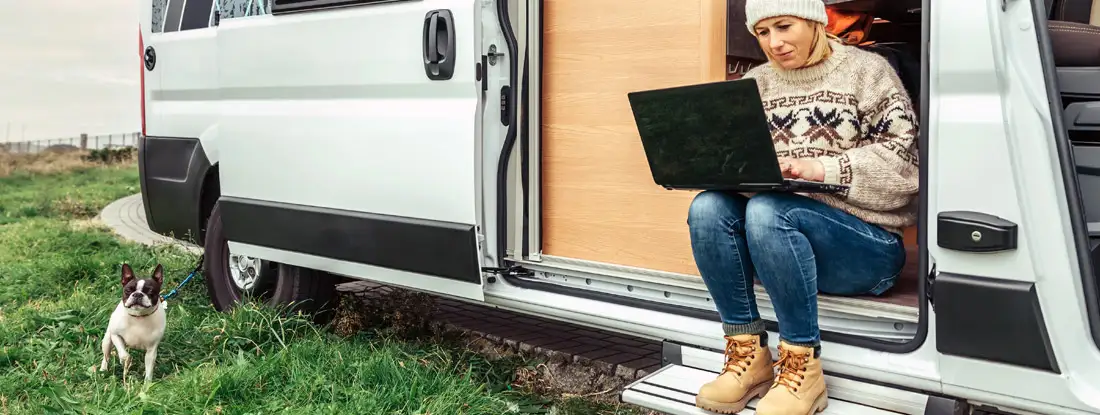 Woman teleworking sitting in the door of a camper van. RV Mechanical Breakdown Insurance. 