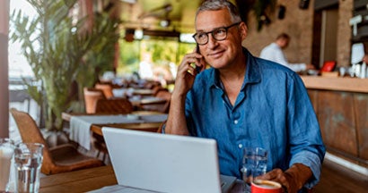 Mature man using smartphone and laptop computer in cafe. How to Buy Business Insurance.