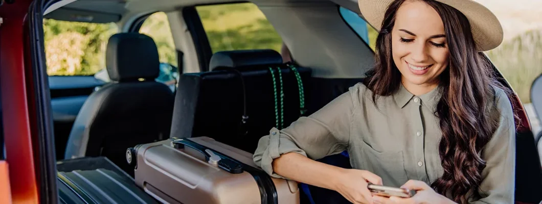 Woman sitting in car trunk full of luggage and using phone. Cody, Wyoming Car Insurance. 