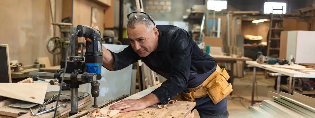 Carpenter using drill press in workshop. Find Cumberland Hill, Rhode Island business insurance.