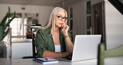 Focused mature woman with white hair at home using laptop