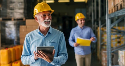 Business owner and employee walking through their warehouse with helmets on their heads. Workers' Compensation Insurance Cost.