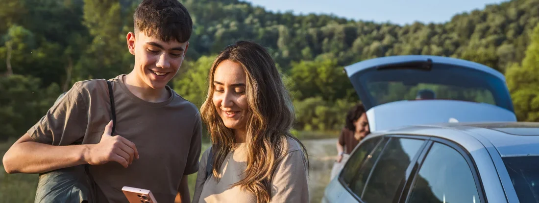 Young man and woman on a break from the road use mobile phone. New Smartphone Apps to Protect Your Teen Driver.