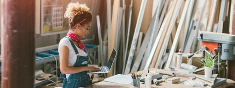 Carpenter standing in her workshop. Holding laptop while she focused on her work.