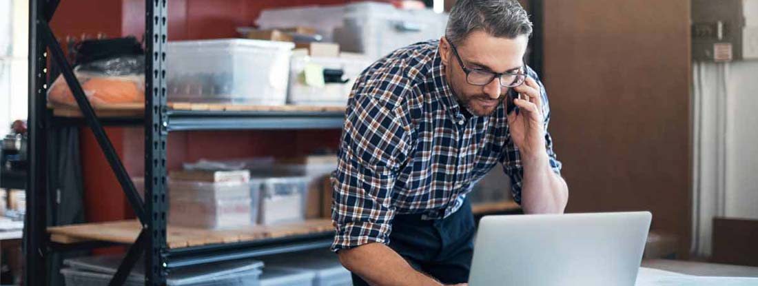 Man using a laptop and mobile phone while working on a project in a workshop. Find LLC Insurance.