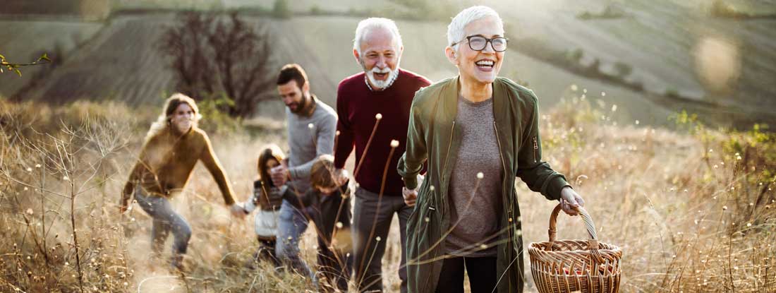 Happy senior couple leading her children and grandchildren to perfect picnic place on the hill. Find Long Term Care Insurance.