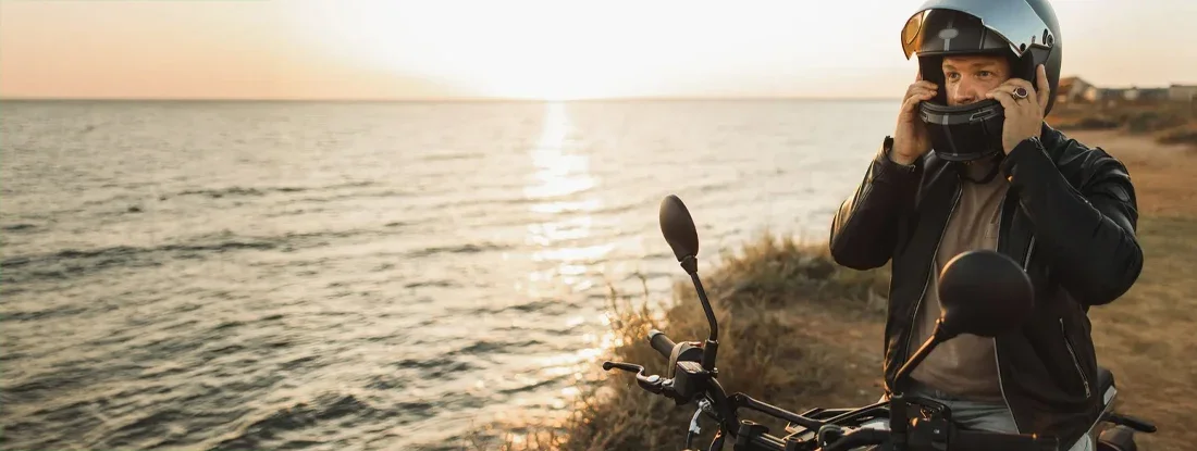 Male biker adjusting helmet, sitting on motorcycle with sunset view. Motorcycle Gear: Protect Yourself from Head to Toe.