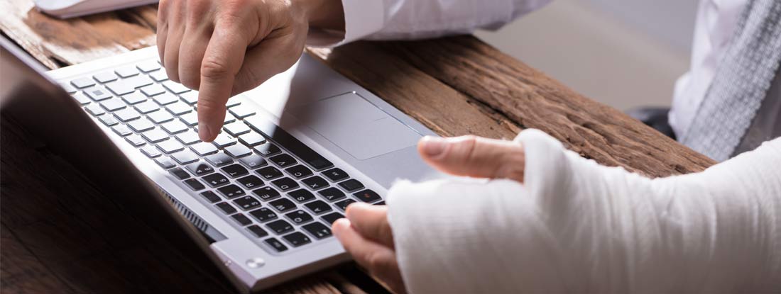Businessperson With Hand Injury Using Laptop. How to Implement a Return to Work Policy.