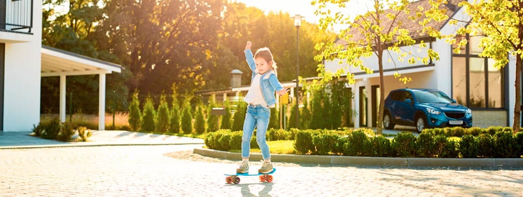 Little girl outdoors near house and car riding skateboard. Find Washington umbrella insurance.