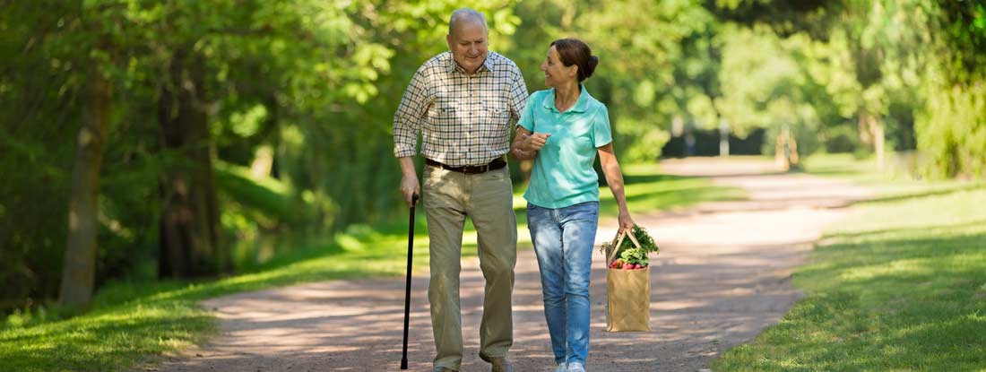 Caregiver helping senior man outdoors in the park. Additional long term care insurance benefits.