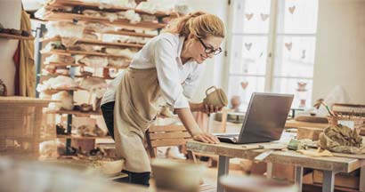 Potter entrepreneur using Shopify on laptop in workshop