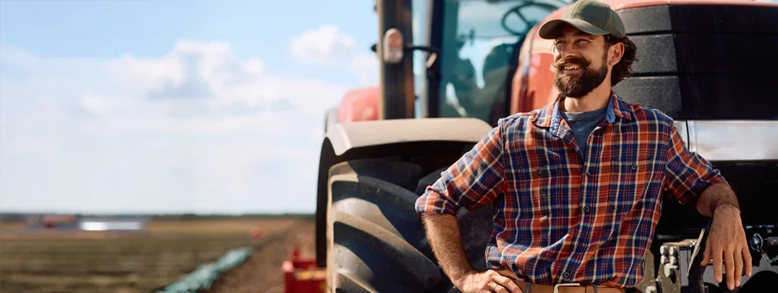 Farm worker leaning on a tractor and looking away. Find Farm and Agricultural Insurance.