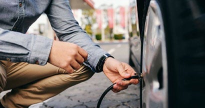 Teen crouching on the gas station and inflating tire. Teens and Tire Safety: What Driver's Ed Doesn't Teach Them. 