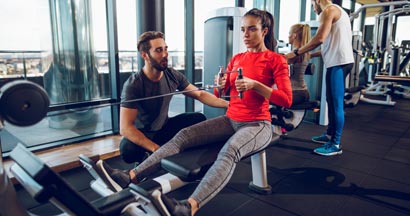 Workout with personal trainer on rowing machine at gym. Find Personal Trainer Insurance.