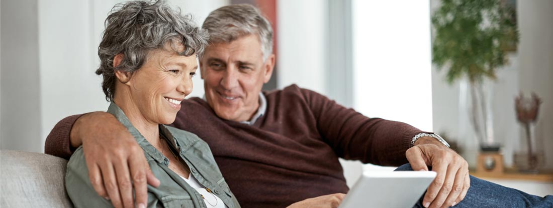 Couple using a digital tablet while relaxing on their sofa. Variable annuities death benefit.