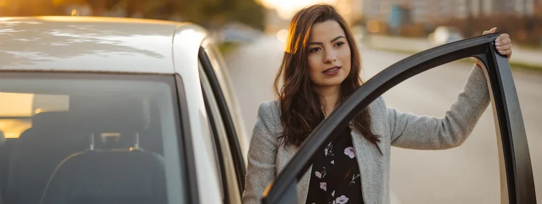 Beautiful young woman getting out of car in the city at sunset. Car Insurance in Montpelier, Vermont.