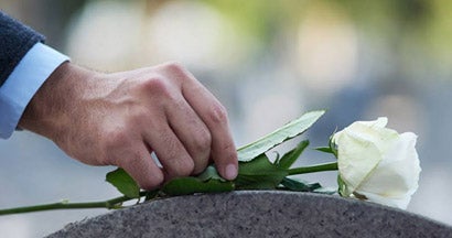 Hand placing a single white rose on a tombstone. Final Expense Insurance.