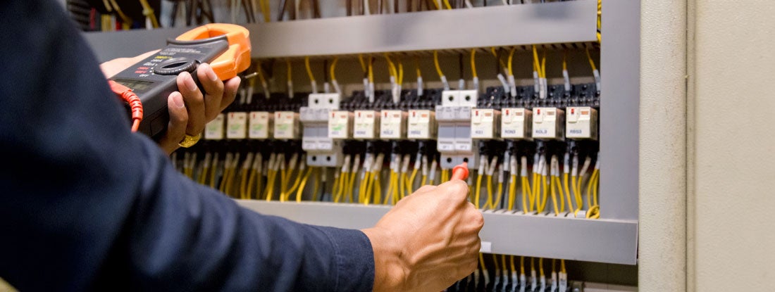 Electrician measuring voltage and current of power electric line in electrical cabinet control. Find electrician license requirements by state.
