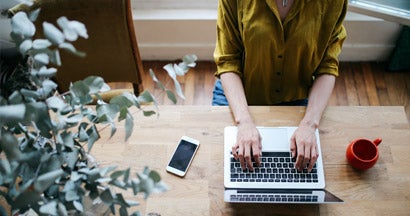 Overhead image of a female small business owner typing on the laptop keyboard. Find small business insurance.