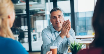 Agent puts his hands together and speaks candidly with an unrecognizable couple. Independent insurance agents vs captive agent.