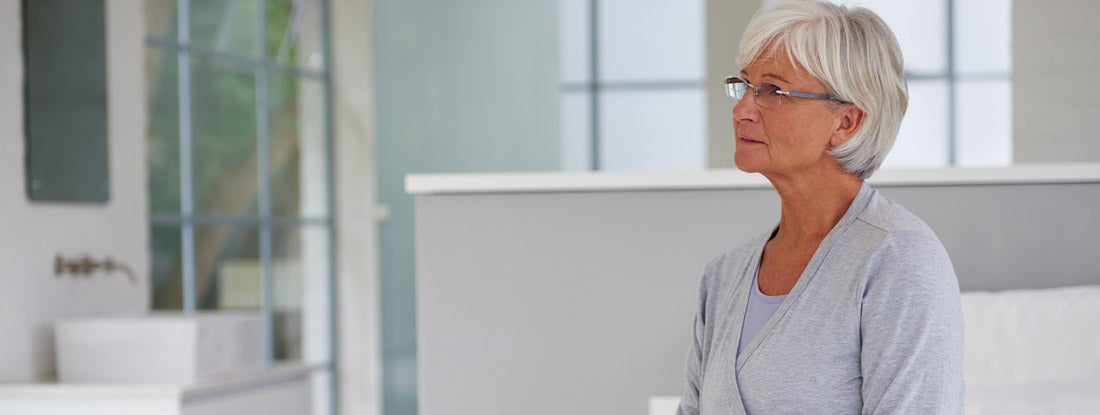 Woman with short gray hair and glasses in waiting room. Critical Illness Life Insurance.