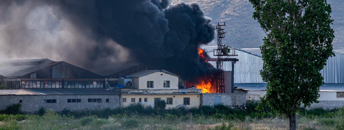 A huge factory fire of black fumes and flames. Time Element Property Insurance.