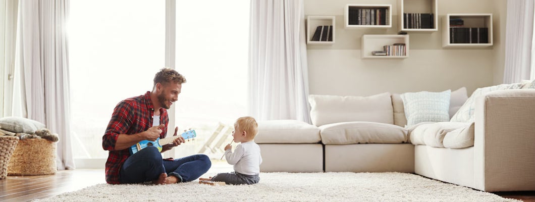 Father playing ukulele with young son in their sitting room. Find Universal Life Insurance. 