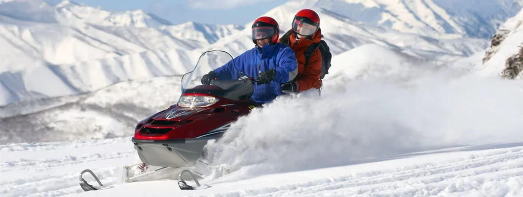 Couple Snowmobiling with Mountains in the background. The Best Snowmobile Destinations in the US.