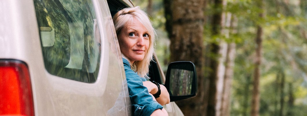 Rear view of a woman in a car leaning at window and smiling. Find Birmingham Michigan car insurance.