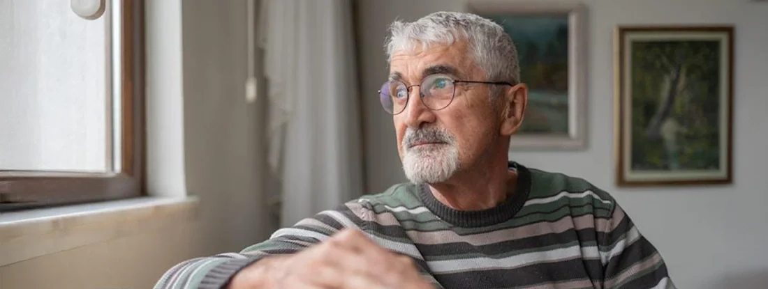 Senior Man Looking Out The Window At Home. HIV Supplemental Health Policy.