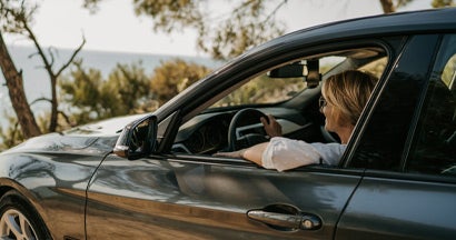 Woman sitting in her car and looking at a beautiful lake. The best cars and SUVs for people with bad backs.